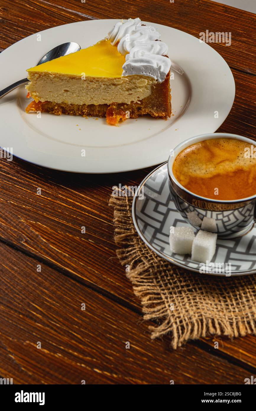 La cheesecake all'arancia appena preparata si siede su un piatto, condita con panna montata. Una tazza di caffè espresso aromatico completa il dessert, promi Foto Stock