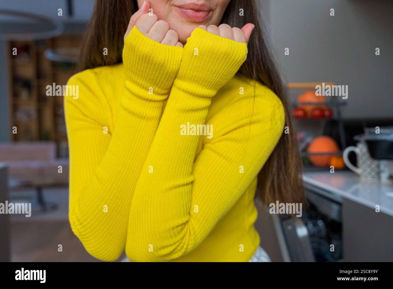 Donna con maglione giallo a maniche lunghe in posa in un'accogliente cucina Foto Stock