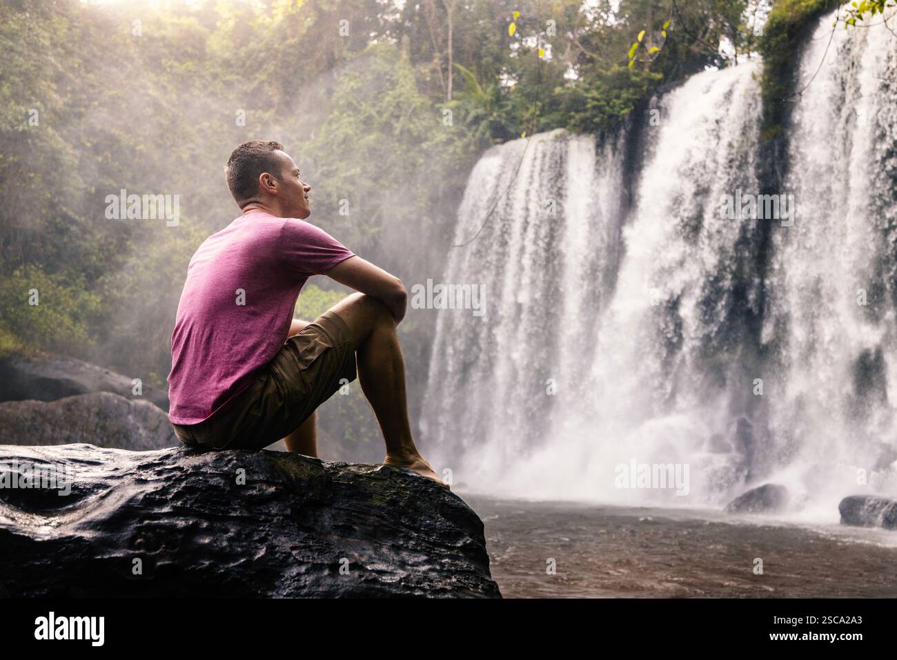Uomo di fronte ad alte cascate in montagna in un paesaggio tropicale. Viaggiatore a Camobodia. Foto Stock