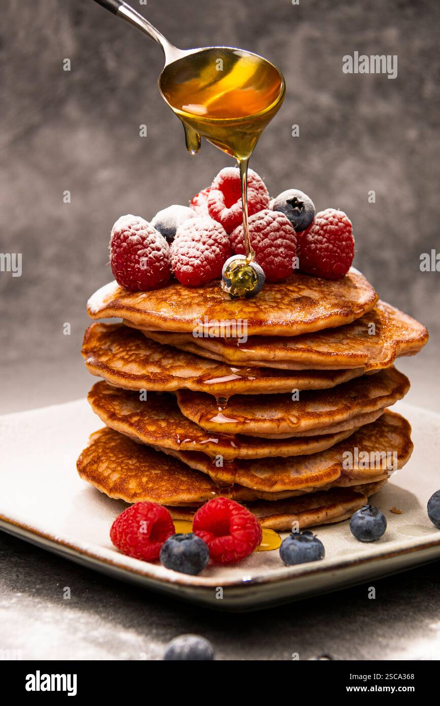 Frittelle con mirtilli e lamponi su un piatto con un cucchiaio con sopra il miele Foto Stock