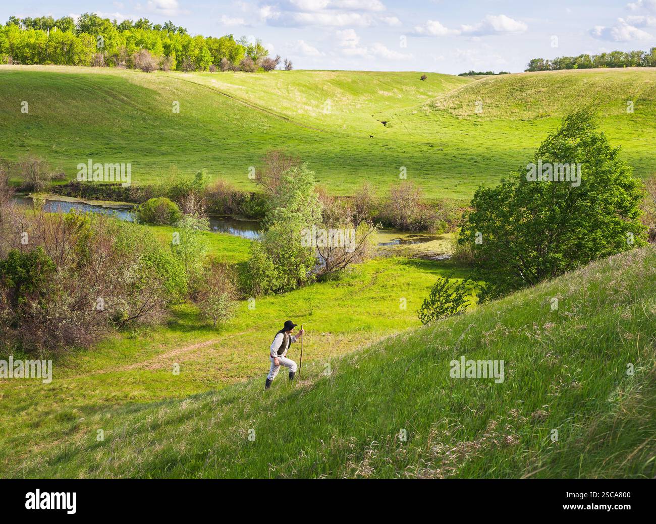 Uomo in cappello nero con una stic sale il pendio di una collina verde Foto Stock