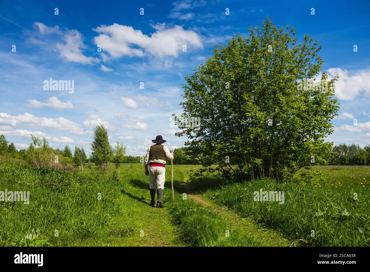 Uomo in cappello nero con una stic sale il pendio di una collina verde Foto Stock