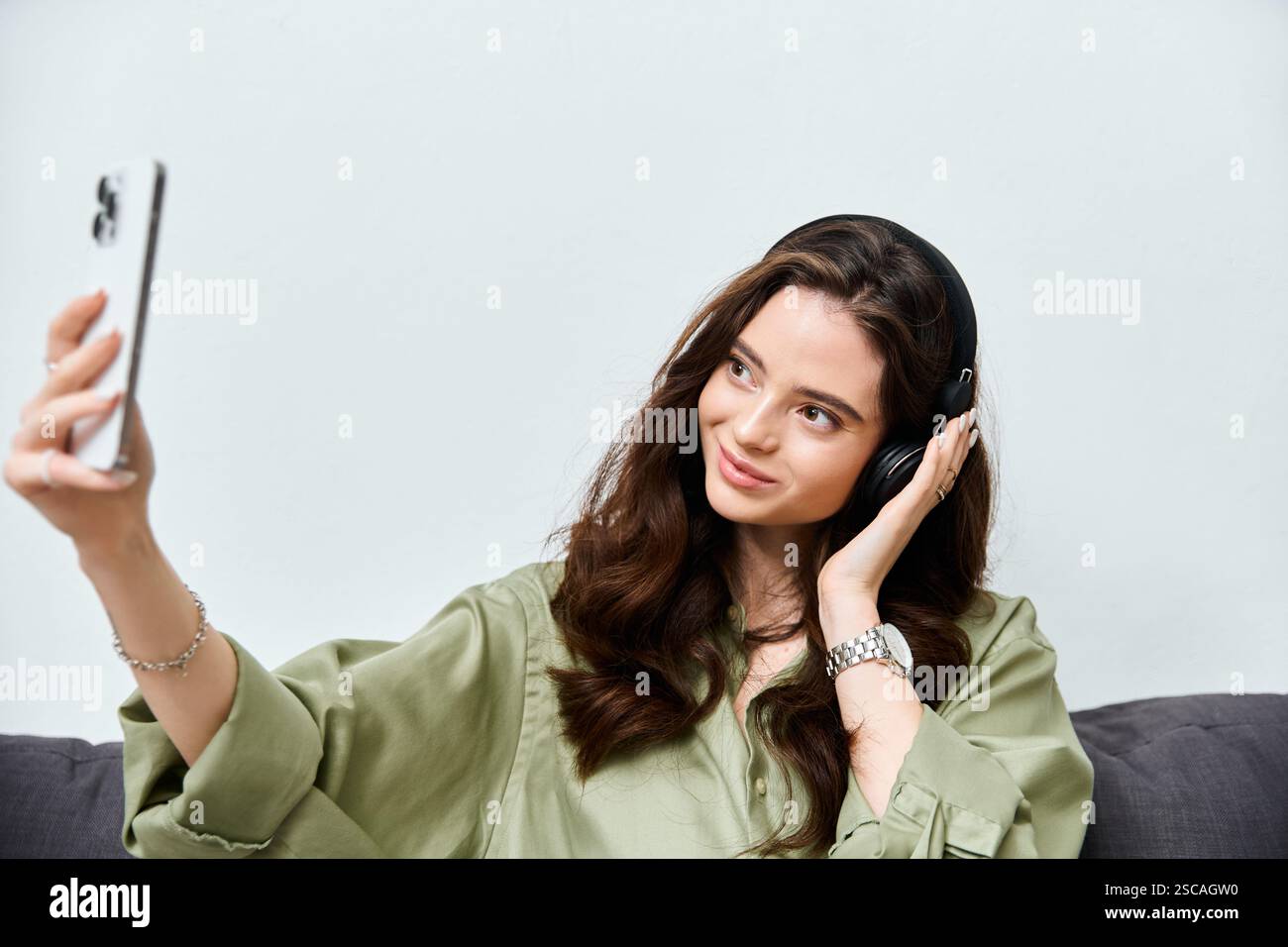 Una giovane donna ama i suoi brani preferiti mentre si fa un selfie a casa, irradiando felicità. Foto Stock