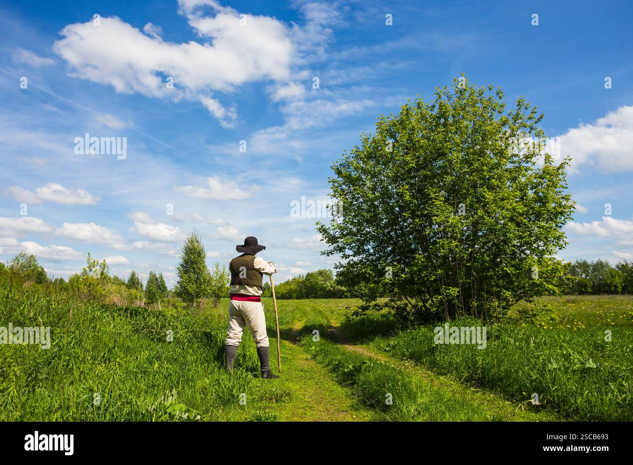 Uomo in cappello nero con una stic sale il pendio di una collina verde Foto Stock