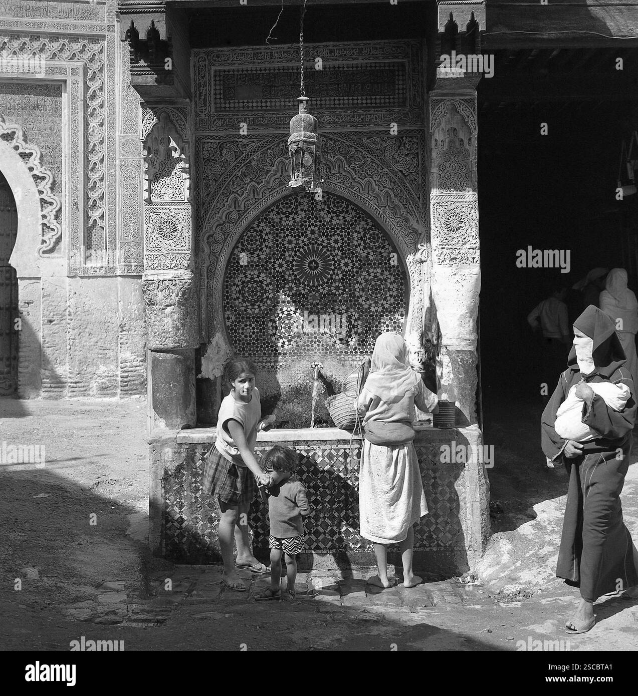 La famiglia a una pubblica fontana e una donna che indossa un burqa in Meknes in Marocco. Foto Stock
