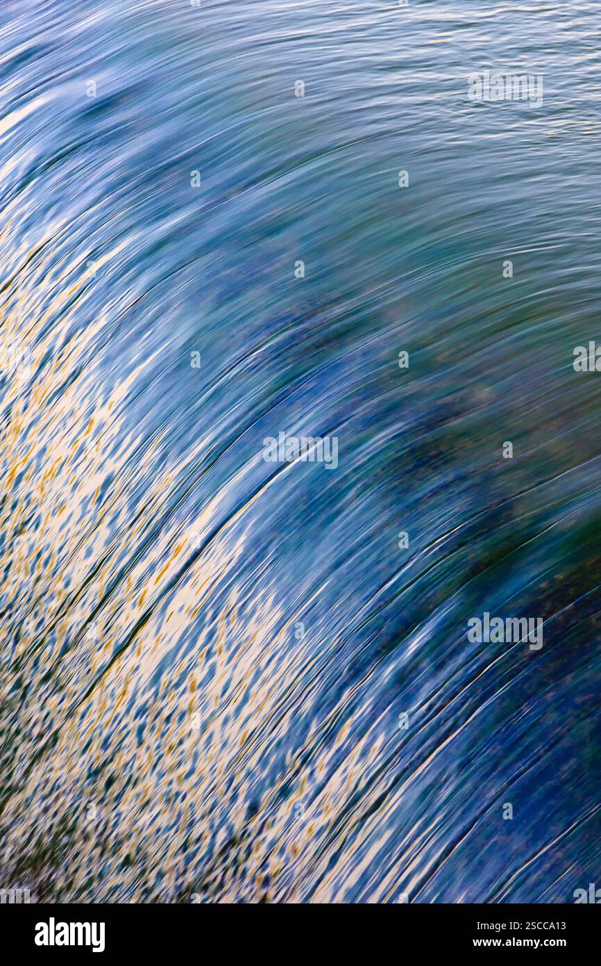 L'immagine è di un corpo d'acqua con una cresta ondulata. L'acqua è blu e l'onda è bianca. L'immagine ha un'atmosfera calma e tranquilla Foto Stock