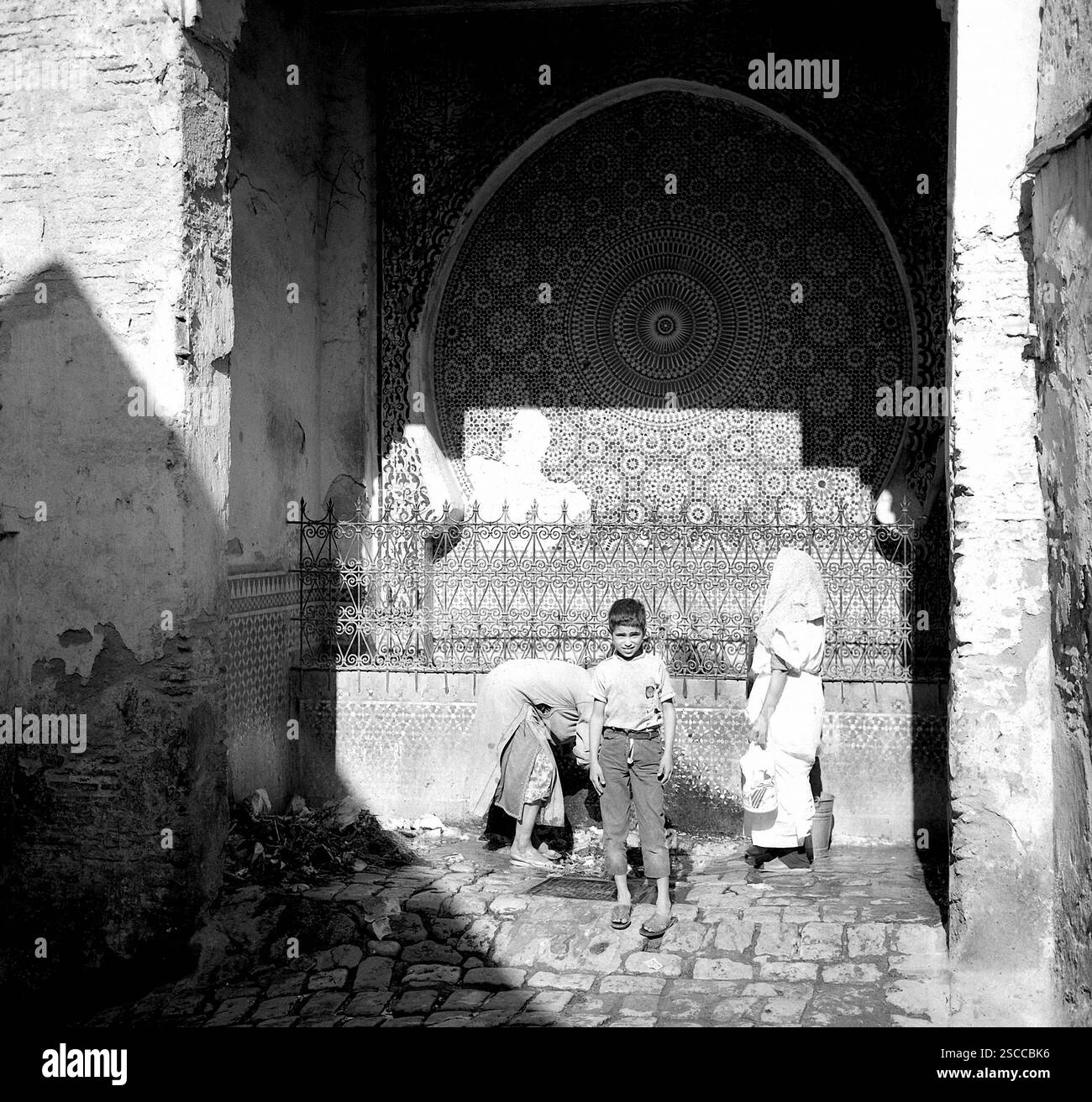 Ragazzo e le donne con velo di ottenere acqua in Meknes in Marocco. Foto Stock