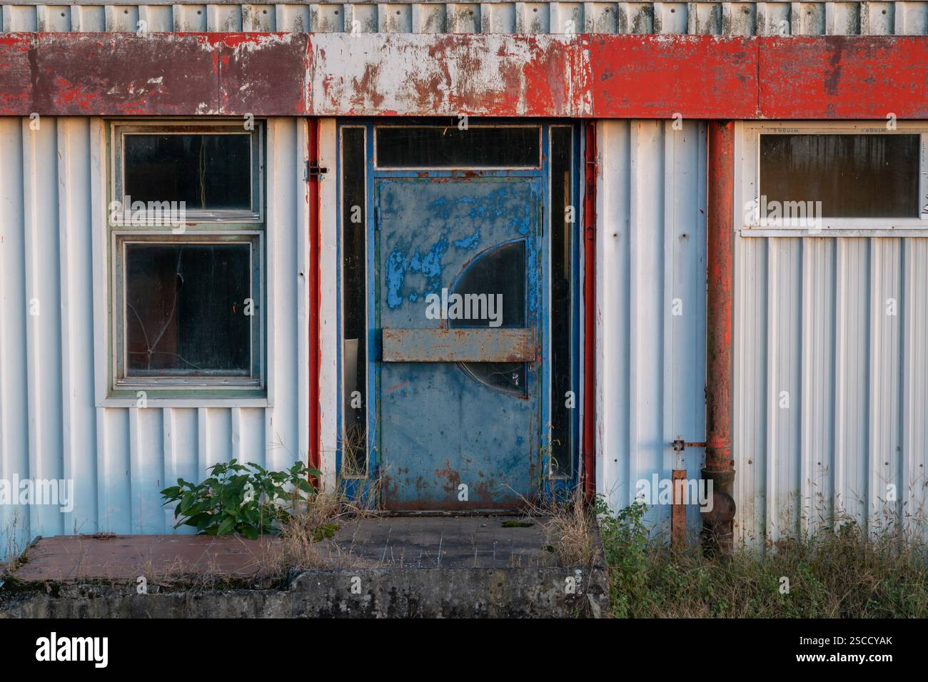 Edificio industriale abbandonato con porte e finestre blu su entrambi i lati, vecchio edificio di panificio in lamiera ondulata Foto Stock
