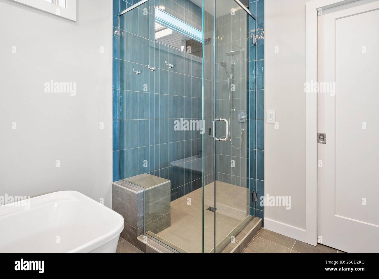 Un bagno con una parete piastrellata blu e una cabina doccia in vetro. Il box doccia è dotato di panca e soffione Foto Stock