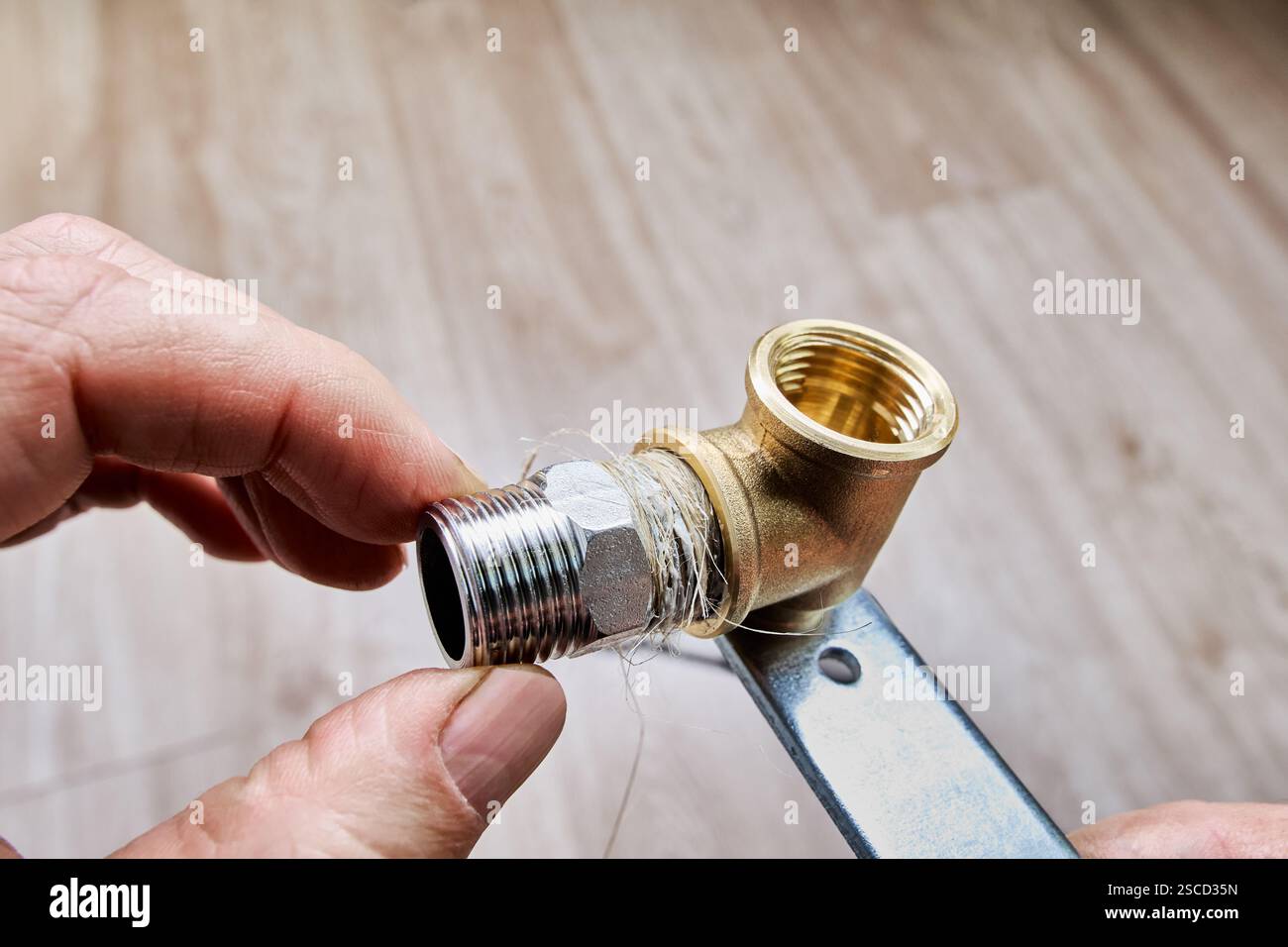 Il lino per tubazioni è avvolto intorno al nipplo riduttore filettato in acciaio inox, preparandolo per l'installazione nel raccordo per tubi in ottone. Foto Stock