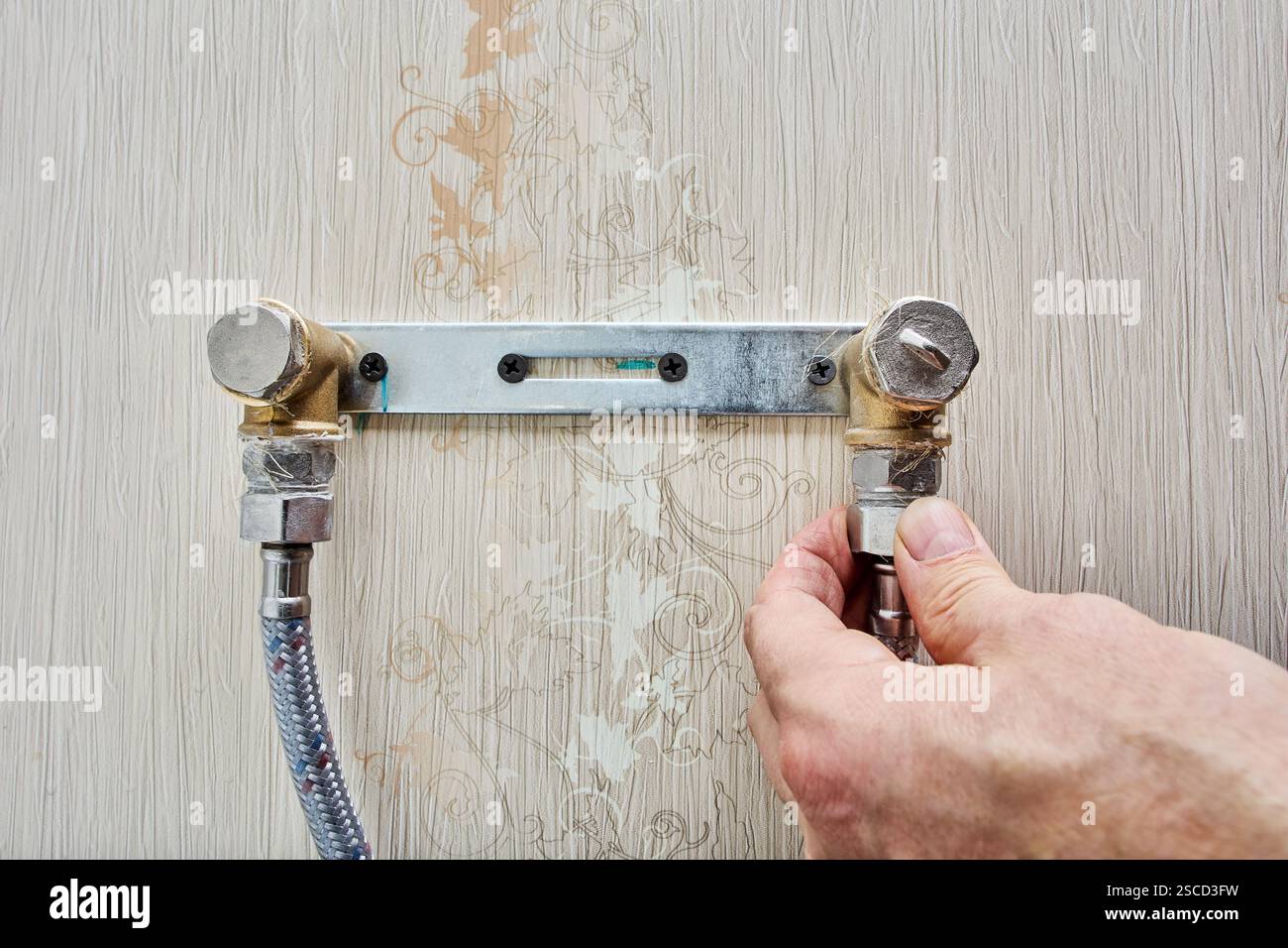 I fori per il fissaggio del rubinetto dell'acqua nella staffa a parete sono coperti da tappi per tubi, tubi flessibili per l'installazione manuale per il montaggio frenato. Foto Stock