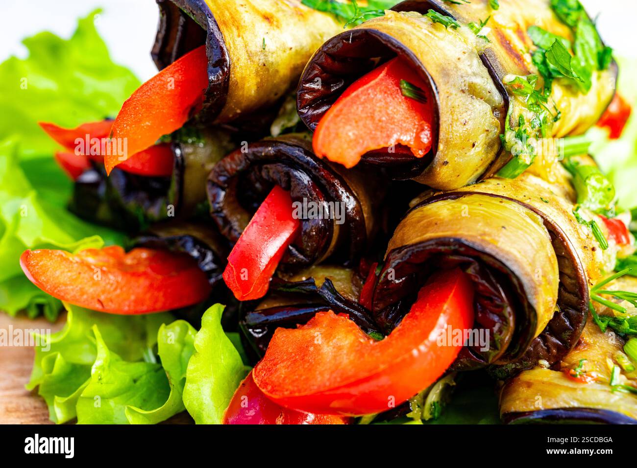 I rotoli di verdure placcati, realizzati con melanzane grigliate e ripieni di peperoni dolci, si trovano su un letto di lattuga croccante. Il piatto presenta un luminoso c Foto Stock
