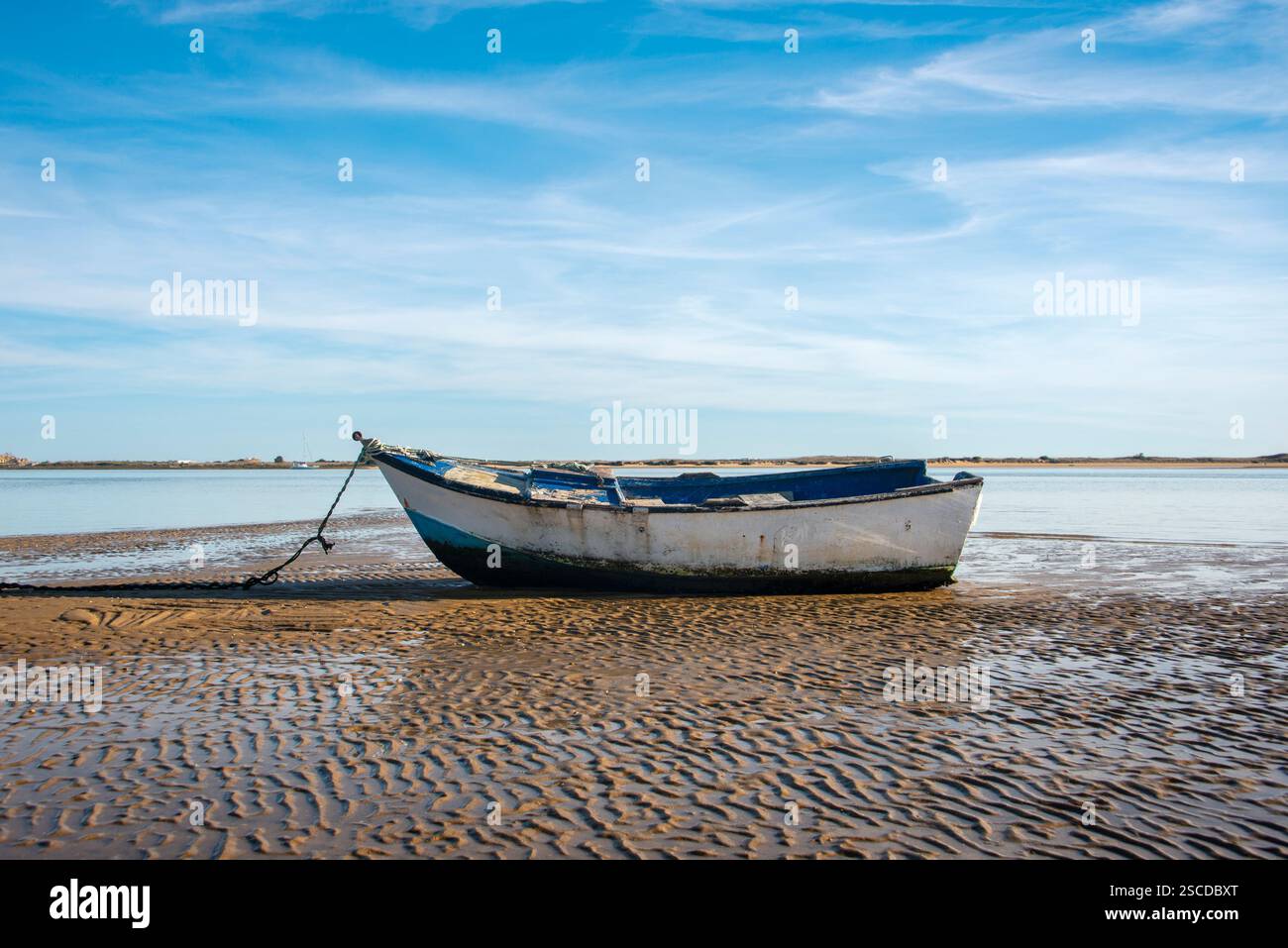 Piccola barca di legno seduta su una spiaggia con bassa marea nell'Algarve. Foto Stock