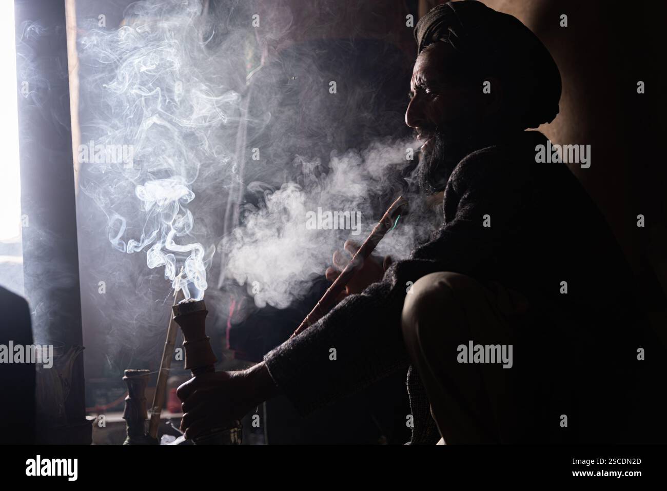 Un uomo afghano sta fumando un chilim (narghilè tradizionale). Foto Stock