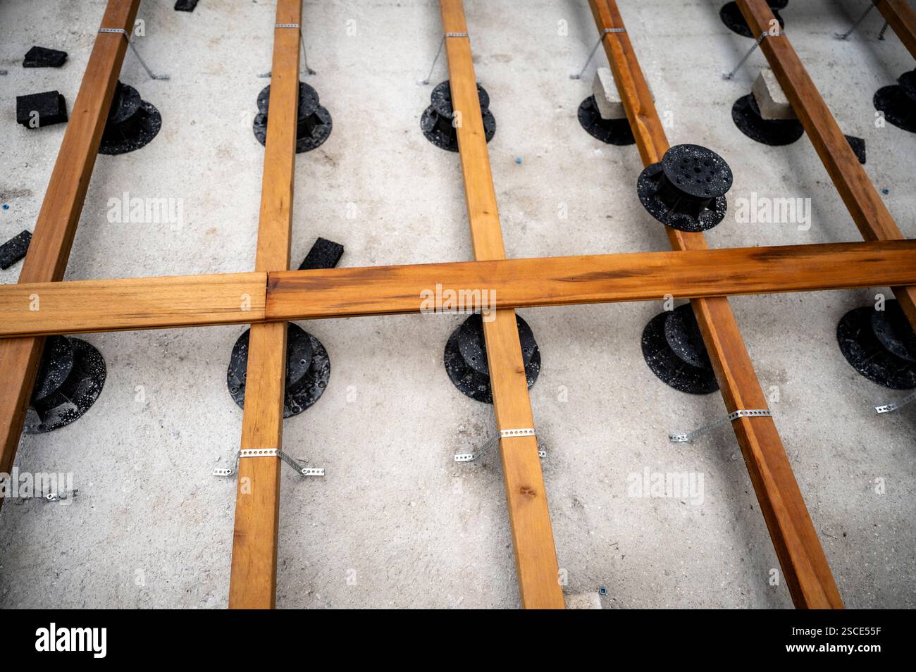 Vista ravvicinata di un telaio del ponte in legno sotto costruzione, sostenuto da piedistalli neri regolabili su una base in cemento, per garantire un foun stabile e uniforme Foto Stock