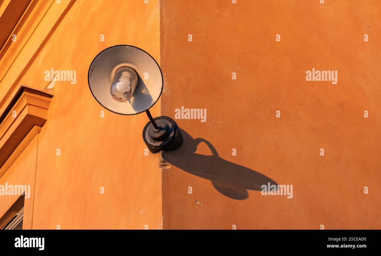 Una vecchia lanterna con un'ombra su una parete arancione al tramonto, che mostra la lanterna com'era ai vecchi tempi Foto Stock