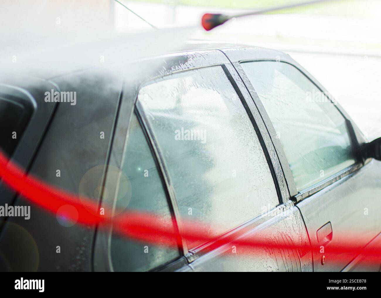 L'auto è in fase di lavaggio con acqua e strisce rosse che si riflettono sul finestrino Foto Stock