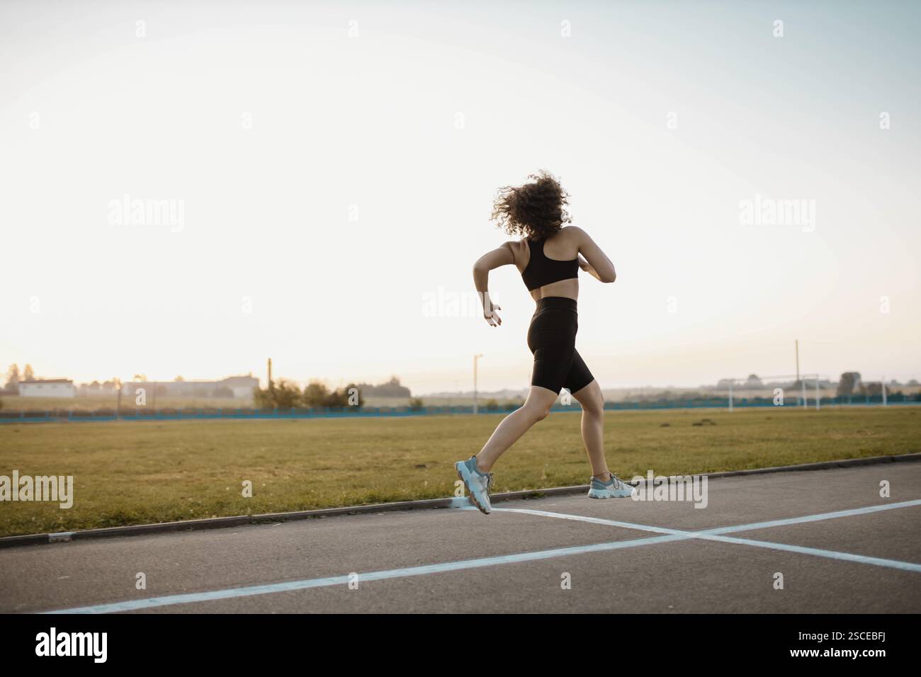 Una donna corre su una pista al tramonto, indossando abiti da ginnastica neri Foto Stock