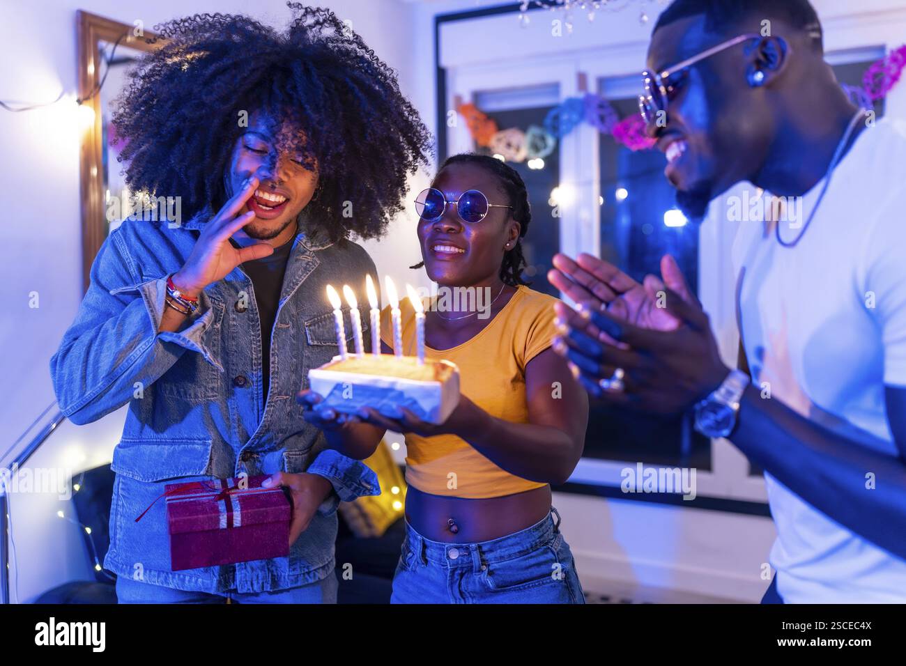 Uomo che fa un desiderio prima di far saltare le candele sulla torta di compleanno con amici multietnici Foto Stock