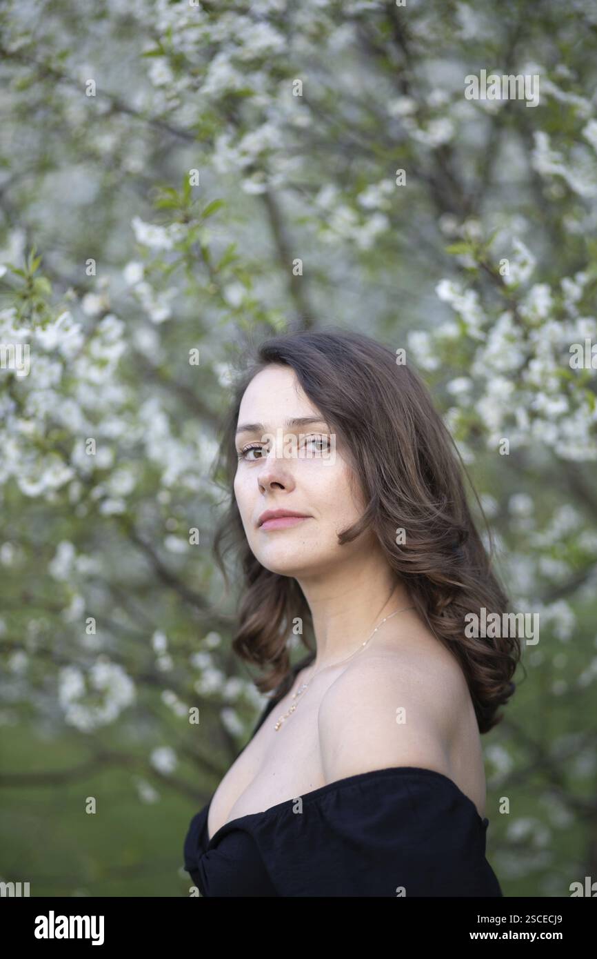 Un sereno ritratto di una donna in un abito nero sullo sfondo di fiori primaverili Foto Stock