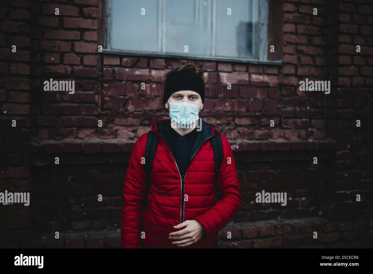 L'uomo con una maschera e un cerchietto si trova di fronte a un muro di mattoni Foto Stock