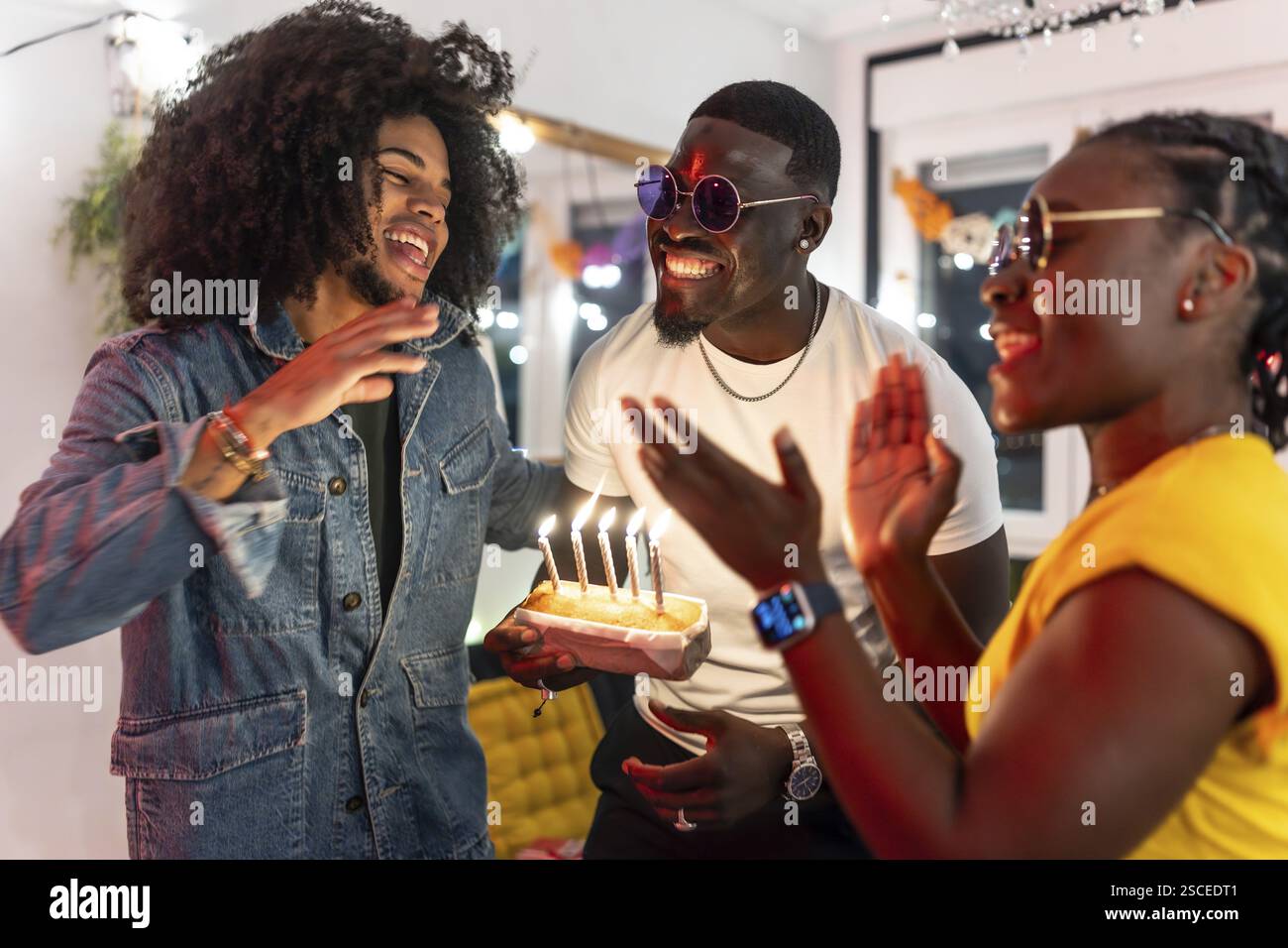 Tanti amici felici che festeggiano il compleanno insieme alla festa a casa cantando la canzone di compleanno e soffiando le candele della torta di compleanno Foto Stock