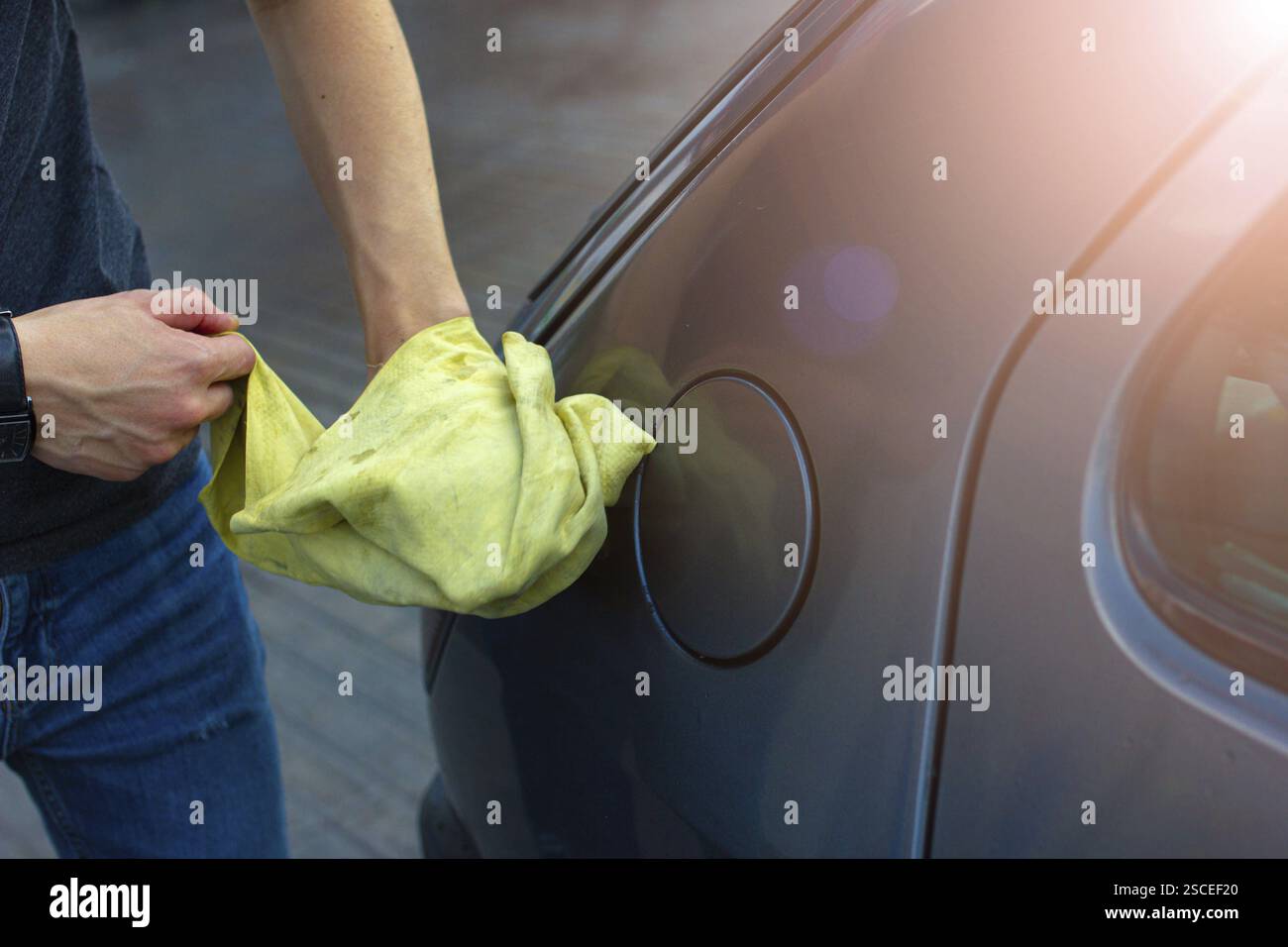 Una persona che pulisce l'area intorno al tappo del carburante di un'auto con un panno giallo Foto Stock