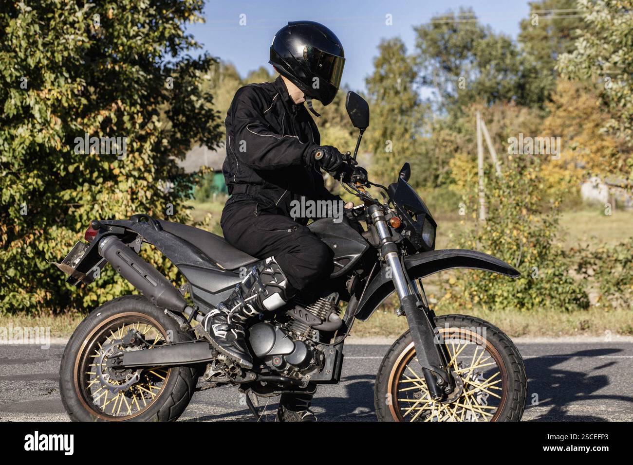 Motociclista in equipaggiamento nero su una bici fuoristrada in campagna Foto Stock