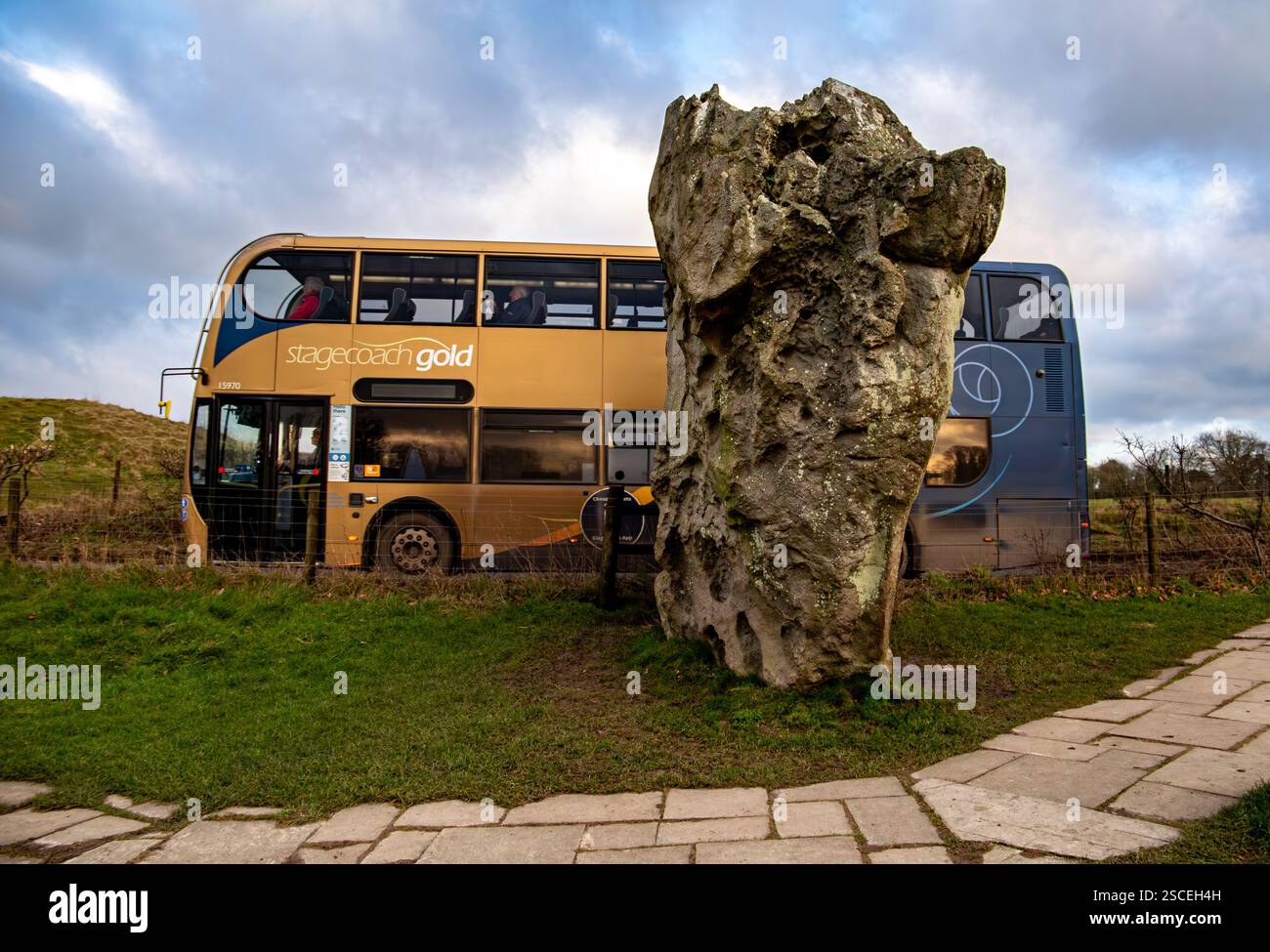 Un autobus a due piani della Stagecoach passa accanto a una grande antica pietra ad Avebury sotto un cielo nuvoloso Foto Stock