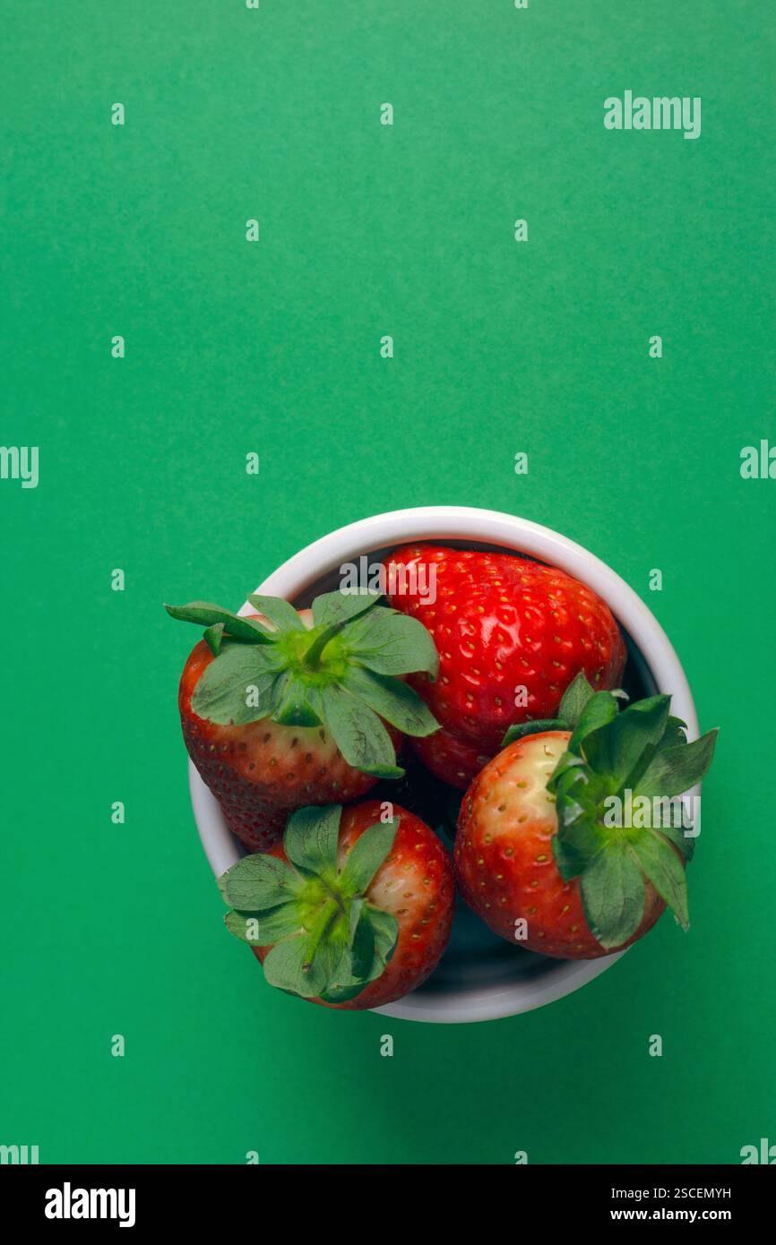 Una ciotola di fragole con foglie verdi. Ci sono quattro fragole nella ciotola. Sfondo verde. Vista dall'alto. Foto Stock