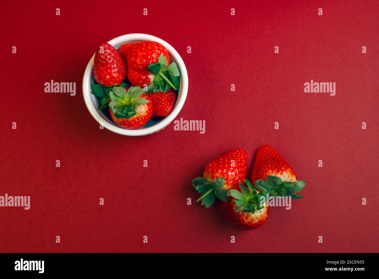 Una ciotola di fragole con foglie verdi. Ci sono anche tre fragole nella parte anteriore. Sfondo rosso. Vista dall'alto Foto Stock