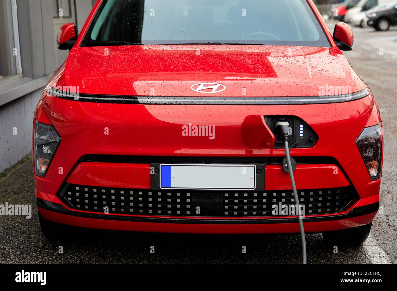 2024 Red Hyundai Kona Electric 2a generazione auto elettrica con batteria collegata a un caricatore da parete, dettaglio anteriore con logo. Salo, Finlandia. 24 gennaio 2025. Foto Stock