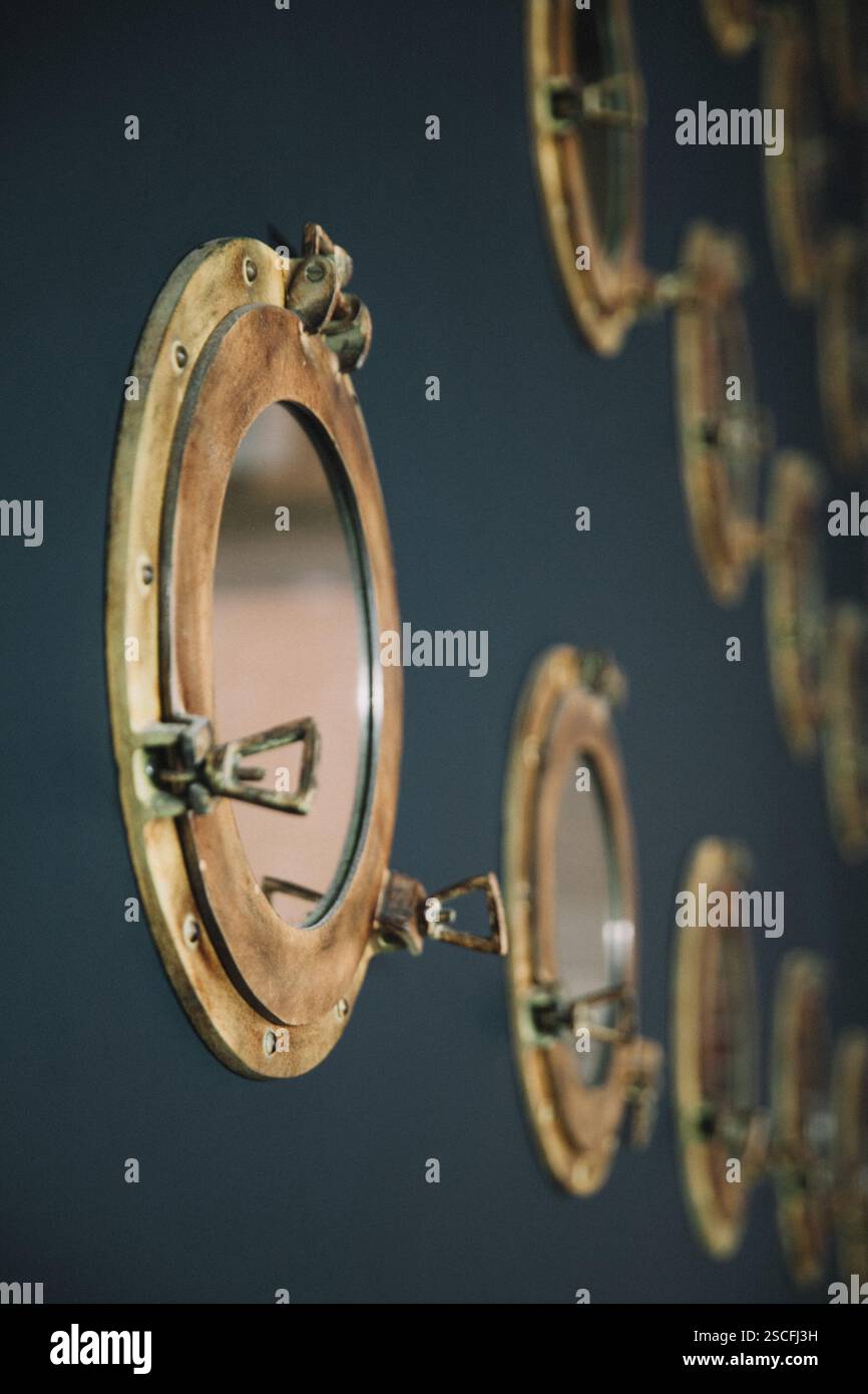 Gli specchi circolari con un telaio in ottone rustico sono montati su una parete scura, riflettendo un'elegante miscela di elementi di design vintage e moderni in questo interi Foto Stock