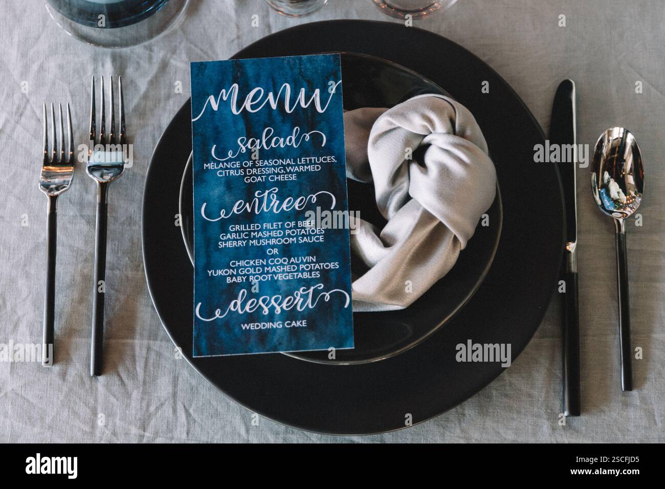 Una sofisticata sala da pranzo presenta un lussuoso piatto nero, argenteria e un menu meticolosamente realizzato per un matrimonio. L'atmosfera è inv Foto Stock