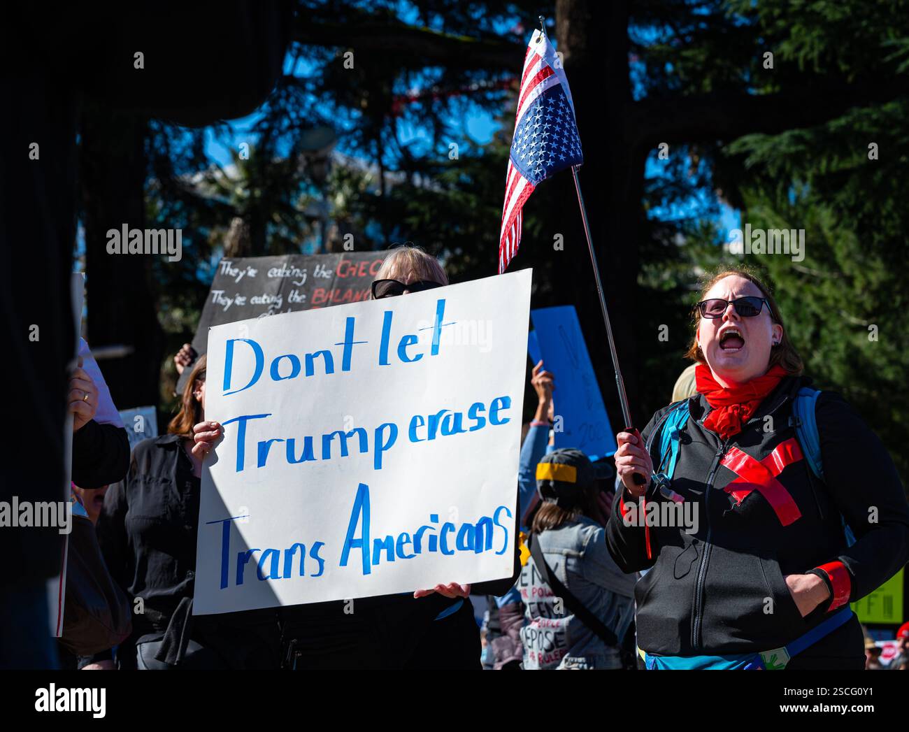 Una donna detiene un Don't let Trump Erase Trans Americans mentre la sua amica tiene una bandiera americana rovesciata alla protesta nazionale anti-Trump del 50501. Foto Stock