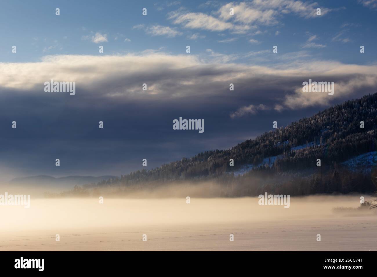 Un lago ghiacciato avvolto dalla nebbia, baciato dall'ultima luce del tramonto. Le montagne sono silenziose, mentre la bellezza dell'inverno si sviluppa in un abbraccio da sogno. Foto Stock