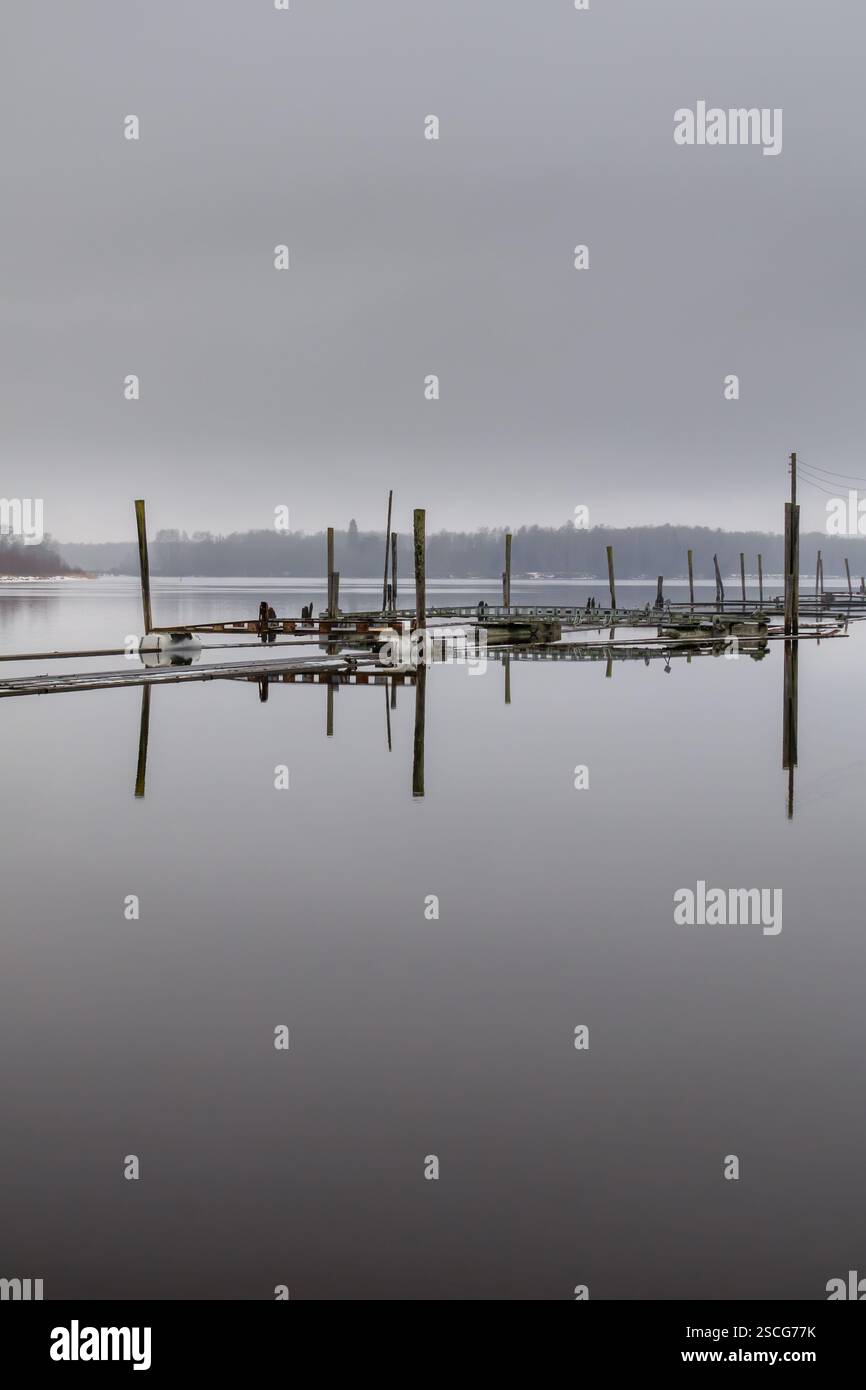 Silenziose e tranquille, le vecchie installazioni idriche sui pontoni si riflettono nelle acque calme sottostanti, resti del passato, riposando sotto un cielo invernale coperto. Foto Stock