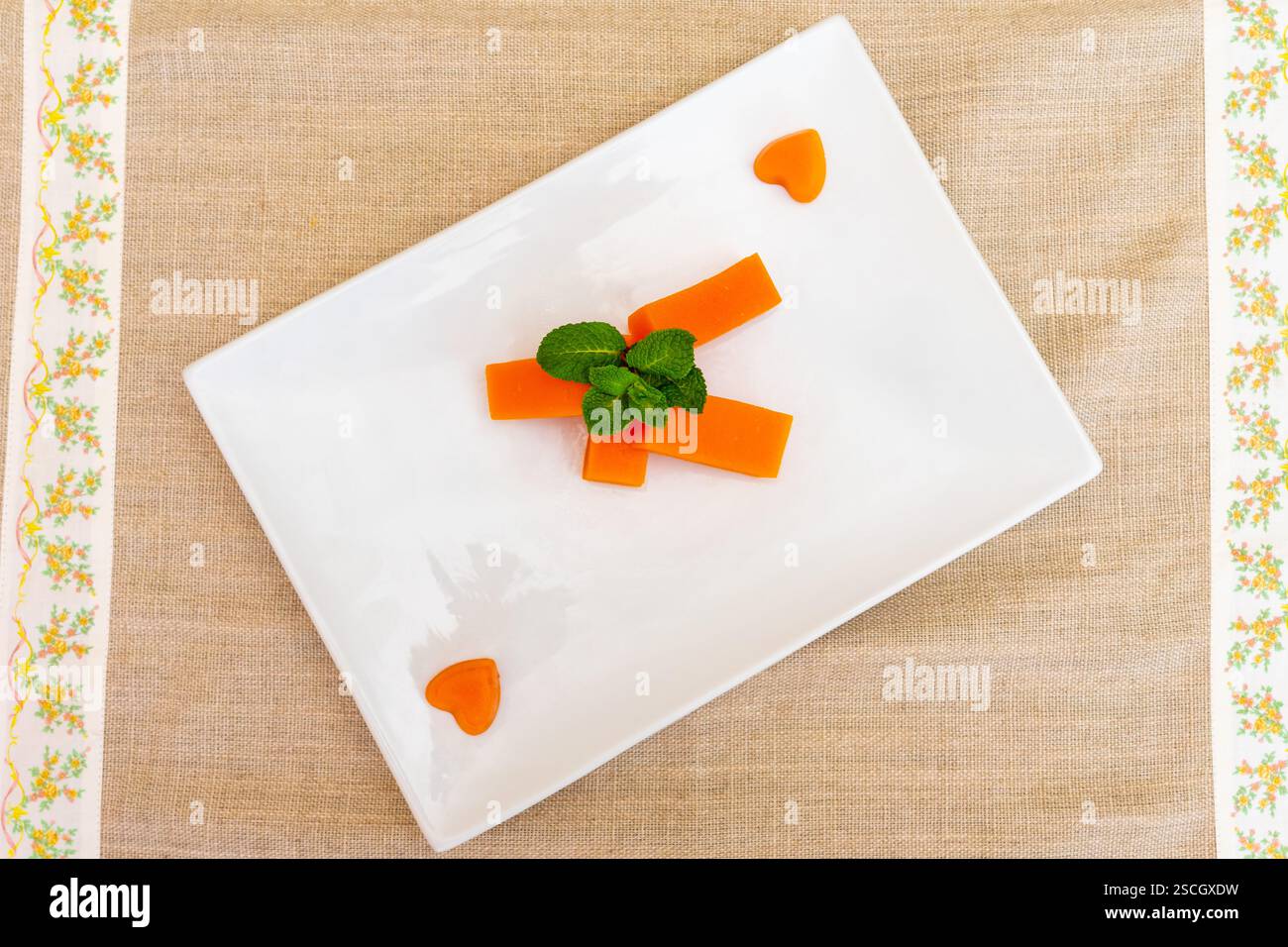 Strisce di carote dai colori vivaci disposte artisticamente su un piatto bianco, guarnite con foglie di menta fresca. I pezzi di carota a forma di cuore aggiungono un tocco divertente Foto Stock
