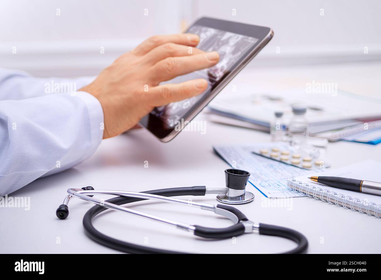 Un operatore sanitario esamina le immagini diagnostiche su un tablet in un ambiente medico, con stetoscopio e forniture nelle vicinanze. Foto Stock