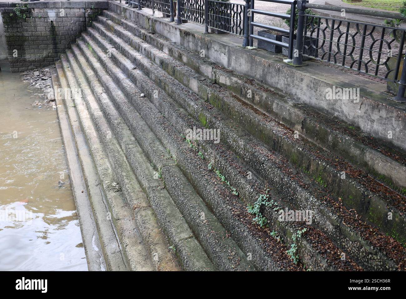 scalini di cemento molto stretti (scale, scale) conducono giù da una spianata lastricata (lungofiume) al livello del fiume Foto Stock