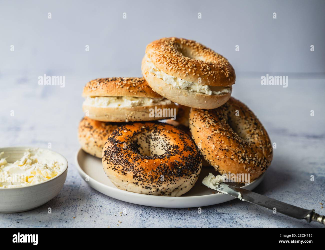 Mucchio di bagel assortiti con formaggio spalmabile su sfondo chiaro. Foto Stock