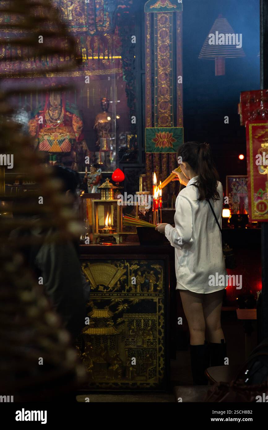 Donna cinese locale, che accende i bastoncini di incenso nel tempio religioso Foto Stock
