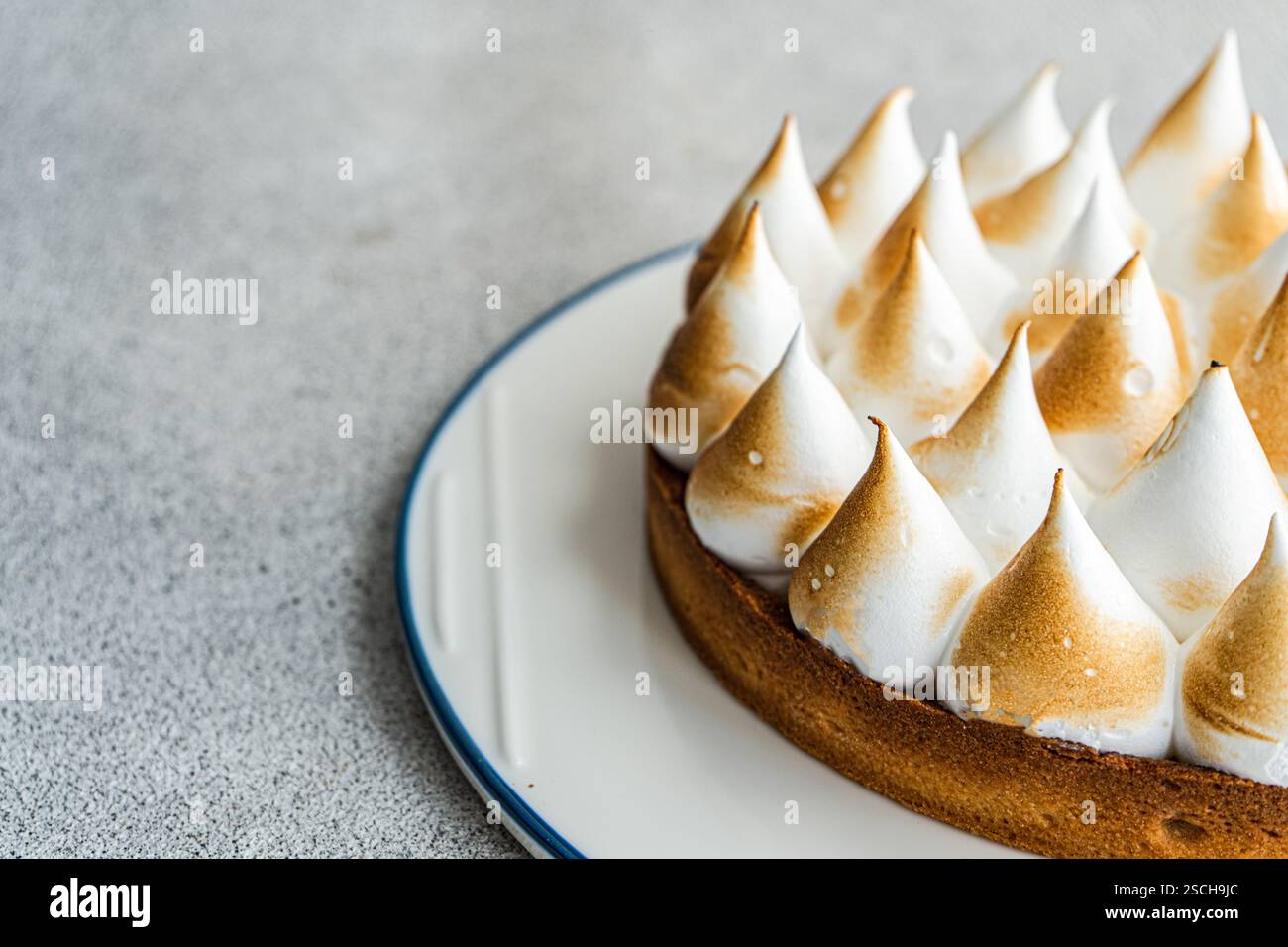 Immagine ravvicinata di una torta al limone fatta in casa, che mostra le sue vette dorate e la crosta burrosa. Il dessert è elegantemente presentato su un piatto bianco agai Foto Stock