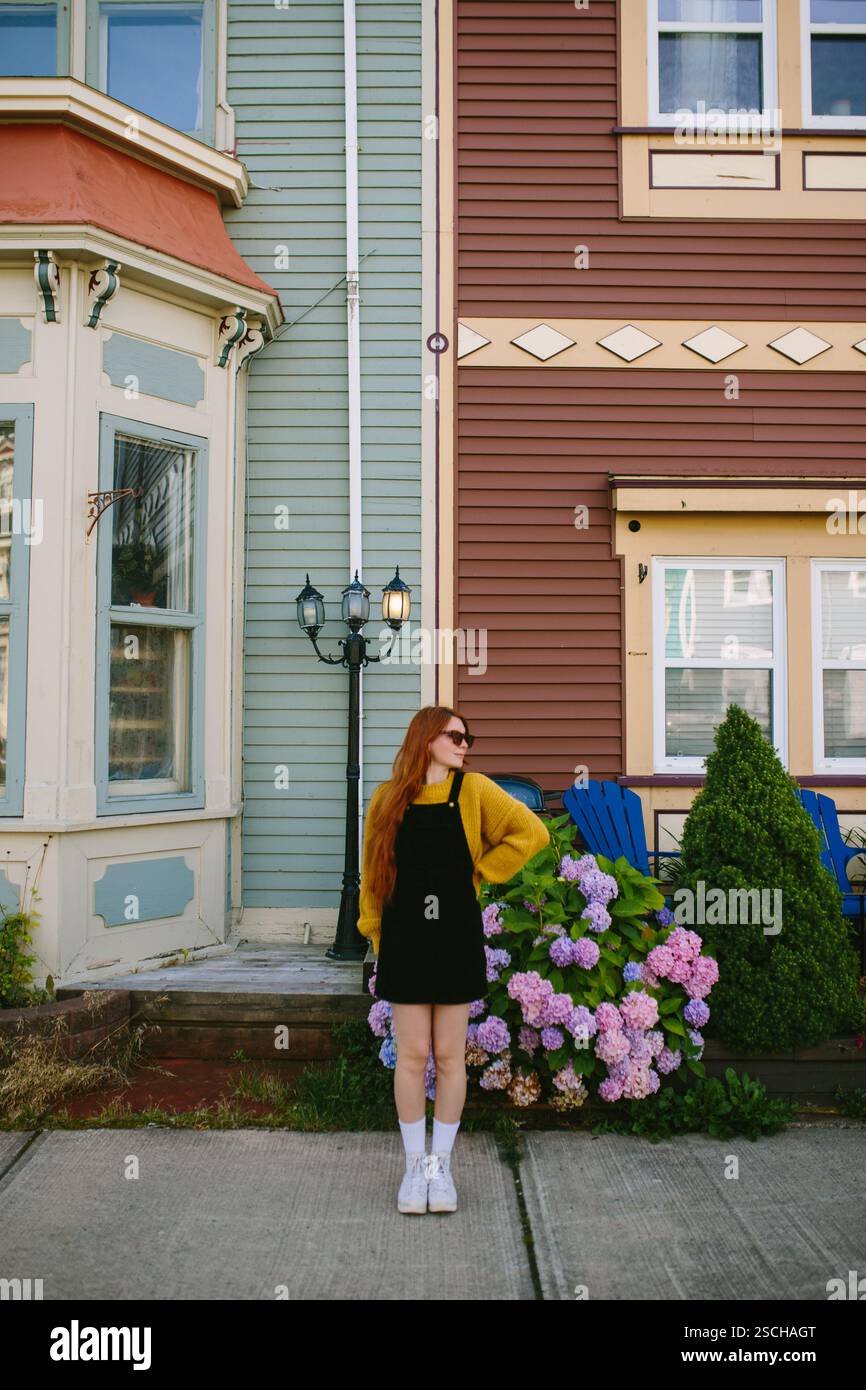 Una giovane donna con i capelli rossi si erge accanto all'architettura classica di St. John's, Newfoundland & Labrador, Canada. Indossato con un elegante abito nero e una Foto Stock