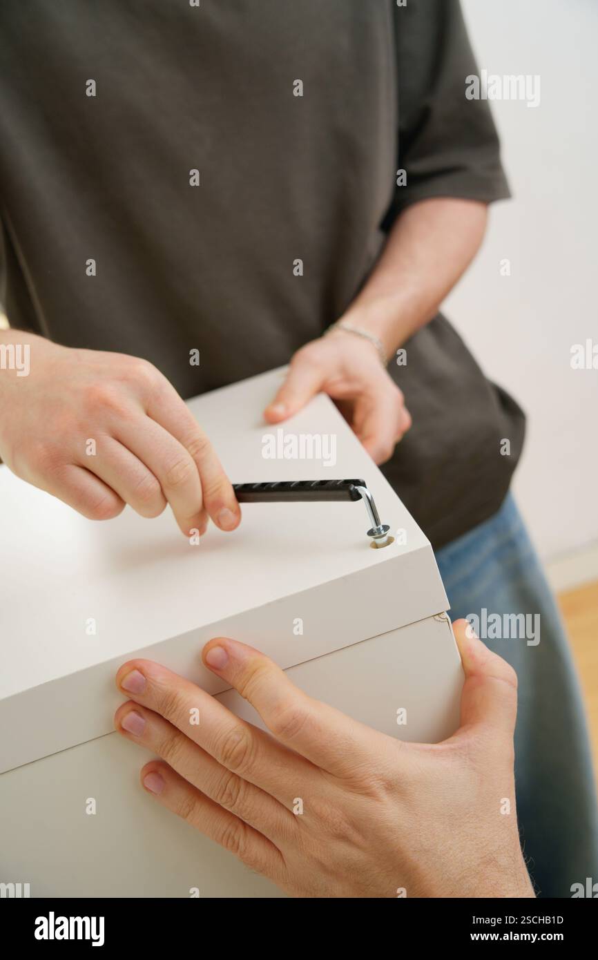 Primo piano ritagliato delle mani di un uomo irriconoscibile utilizzando strumenti per assemblare un nuovo mobile, concentrandosi sul lavoro manuale coinvolto e sui dettagli della Foto Stock