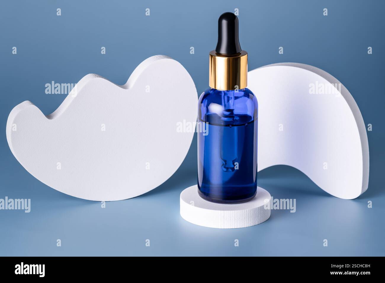 Elegante bottiglia in vetro blu con contagocce su un podio bianco geometrico su sfondo blu Foto Stock