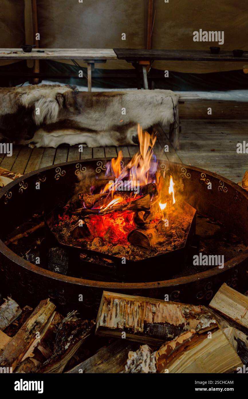 Fuoco caldo e invitante in un ambiente scandinavo nella Lapponia svedese. I tronchi di legno sono pronti per essere bruciati, creando un'atmosfera accogliente. Foto Stock