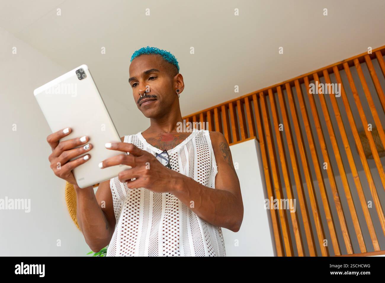 Un uomo LGBTQIA+ abbraccia lo spirito natalizio, coinvolgendo un tablet in un ambiente caldo e invitante. Una celebrazione della diversità e della gioia nella preparazione delle vacanze Foto Stock