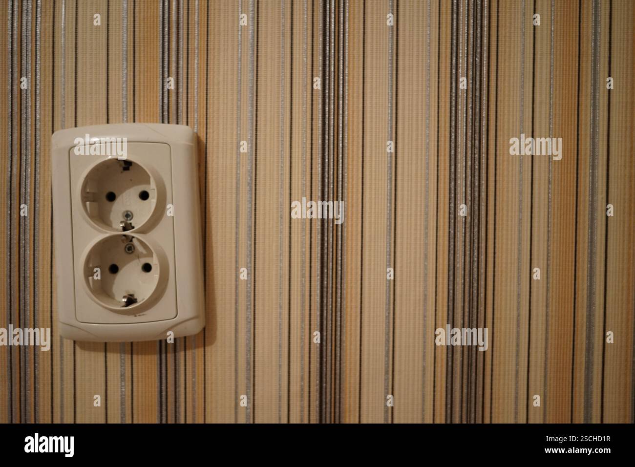 Una presa a muro è visibile sullo sfondo di una carta da parati a strisce. La presa è dotata di due prese e sembra essere in buone condizioni, contribuendo al Foto Stock