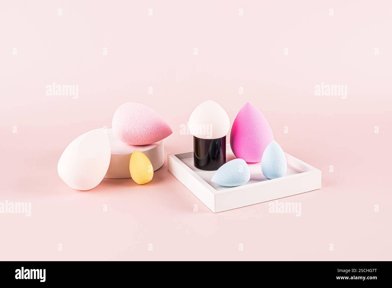 Un assortimento di spugne per il trucco vivaci e colorate del frullatore di bellezza visualizzate elegantemente su sfondo rosa, che offrono una scelta di forme per un look di bellezza Foto Stock